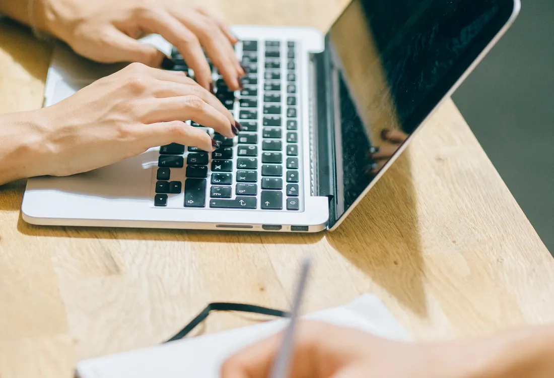 Hands using a laptop and writing notes at a desk