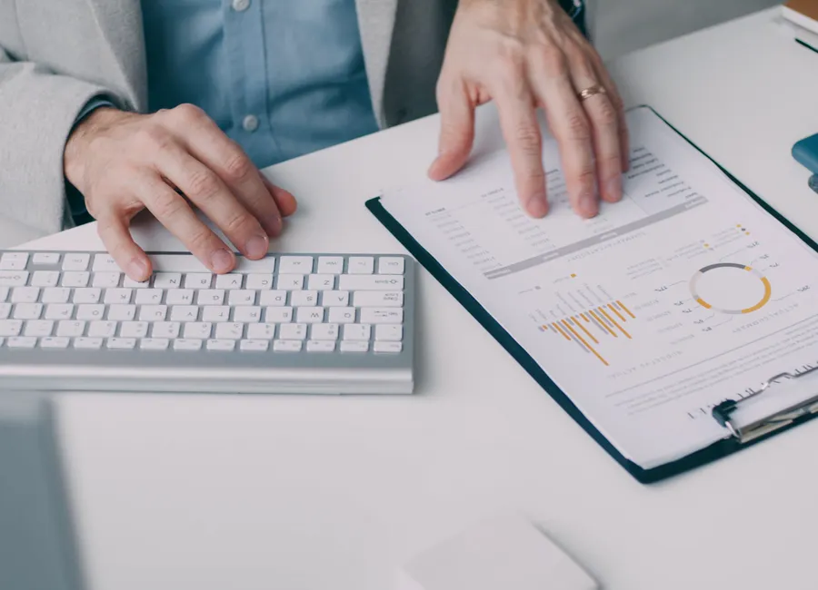 Hands reviewing a printed financial report beside a keyboard