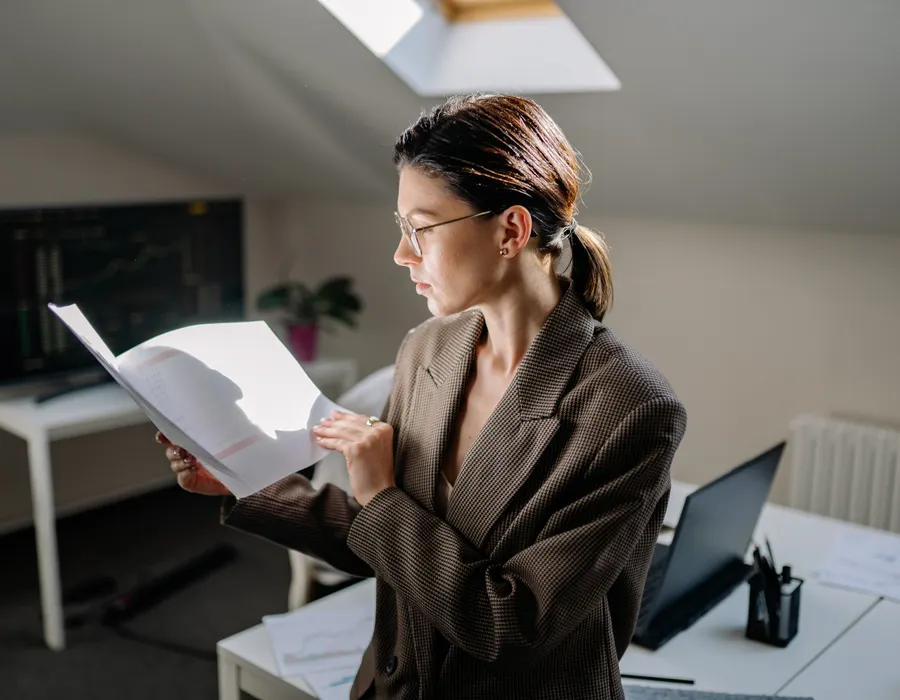 A woman reviewing printed documents beside a laptop