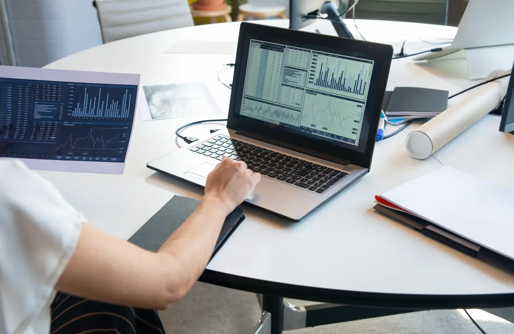 A person comparing printed charts with data on a laptop
