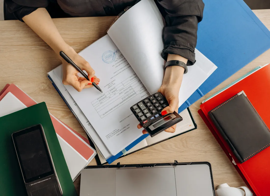 Hands reviewing financial documents beside a calculator and laptop